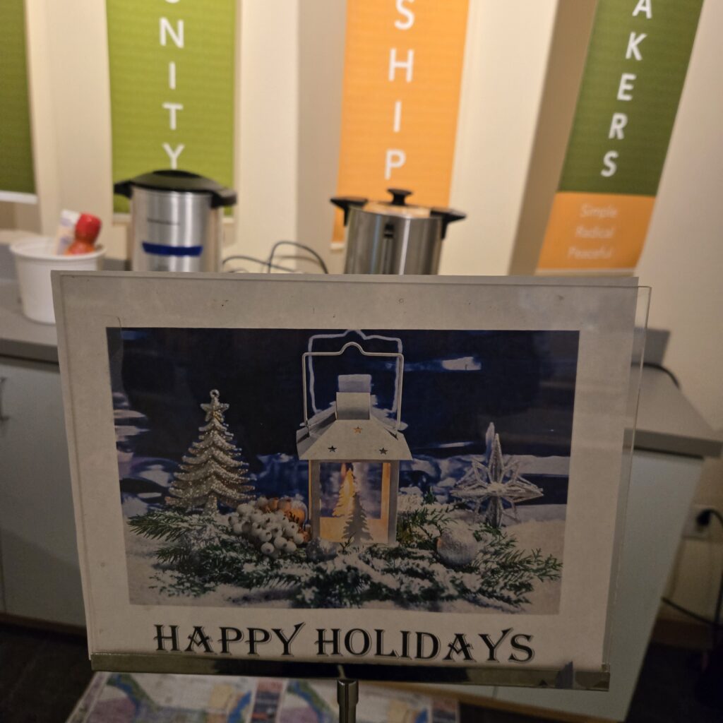 A sign says Happy Holidays with a seasonal graphic. In the background are urns for coffee and hot water.