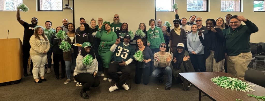 A group of people, many in green and several in Eagles wear, cheer, "Go Birds!" They are tenants of Friends Center.