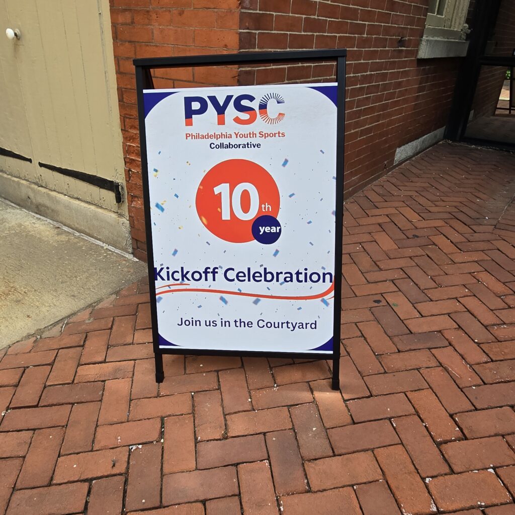 A sign board in front of Friends Center. It says PYSC. Philadelphia Youth Sports Collaborative 10th year kickoff celebration. Join us in the courtyard.