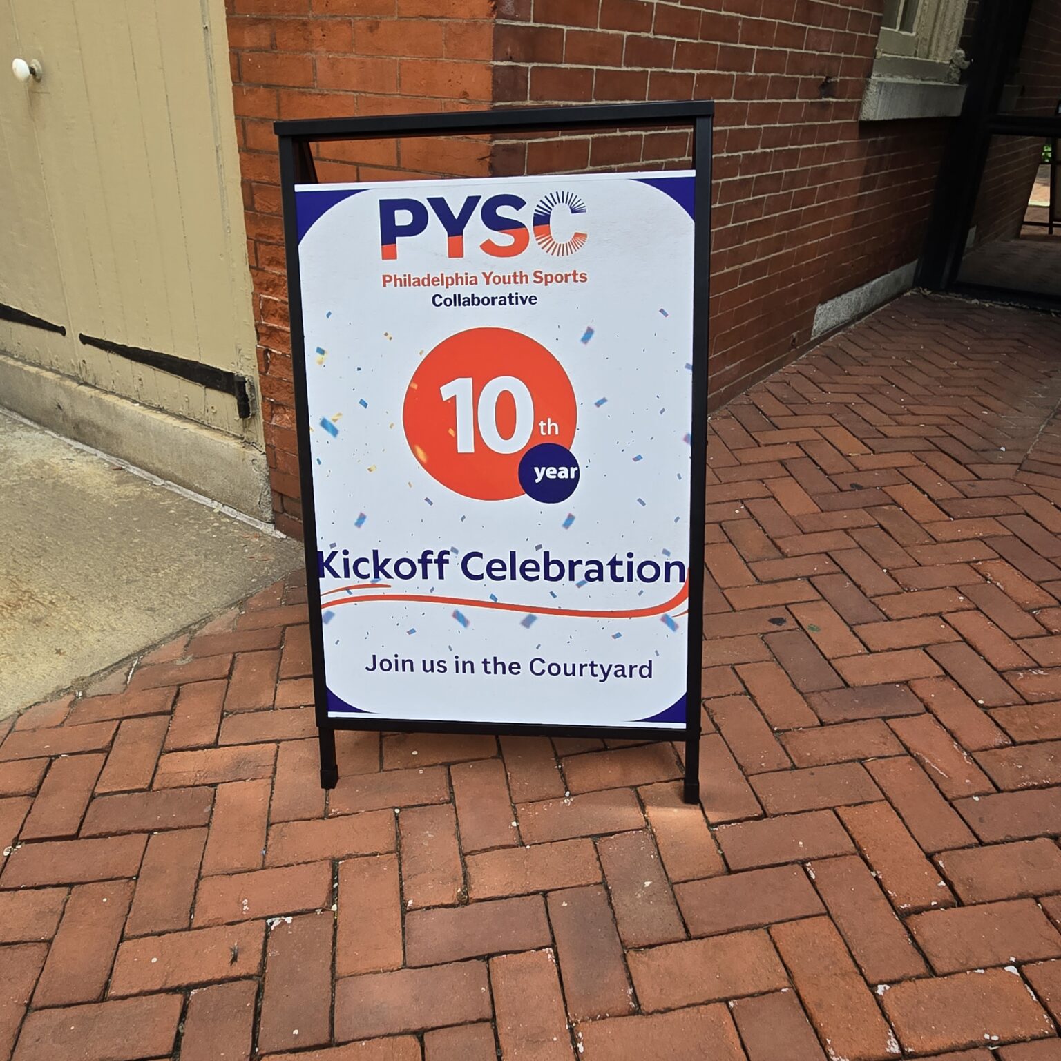 A sign board in front of Friends Center. It says PYSC. Philadelphia Youth Sports Collaborative 10th year kickoff celebration. Join us in the courtyard.