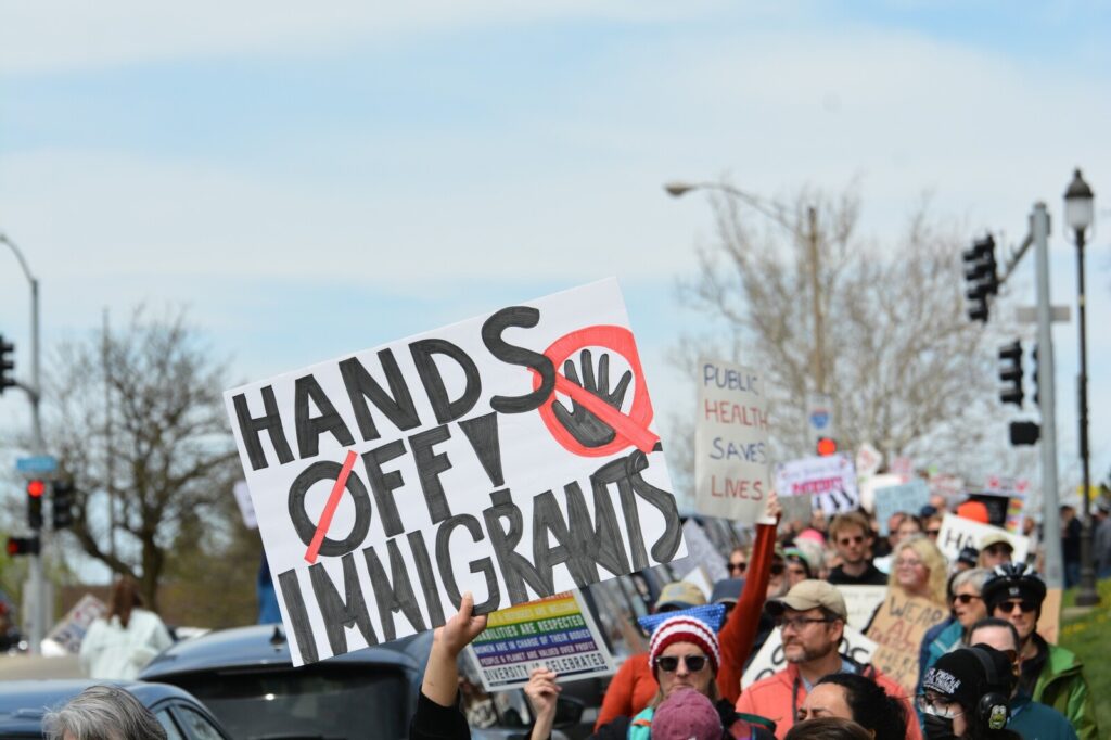 A crowd of a people at a rally. One sign says, "Hands off immigrants."