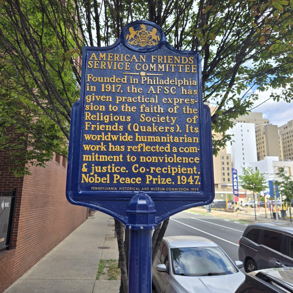 Blue historical marker with yellow text says, "American Friends Service Committee. Founded 1917. Co-recipient of Nobel Peace Prize, 1947."